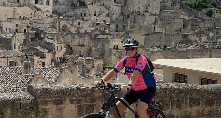 Cycliste solitaire pose sur un vélo électrique avec vue panoramique sur les maisons de pierre de Matera en arrière-plan.