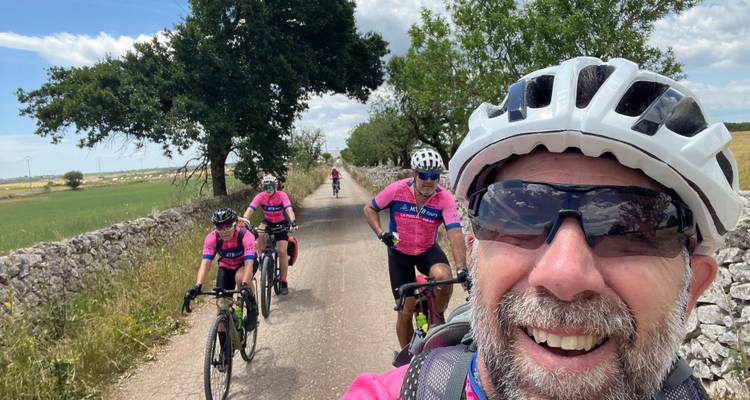 Un cycliste prend un selfie joyeux pendant que ses amis le suivent le long d'un chemin de campagne bordé de murs de pierre.