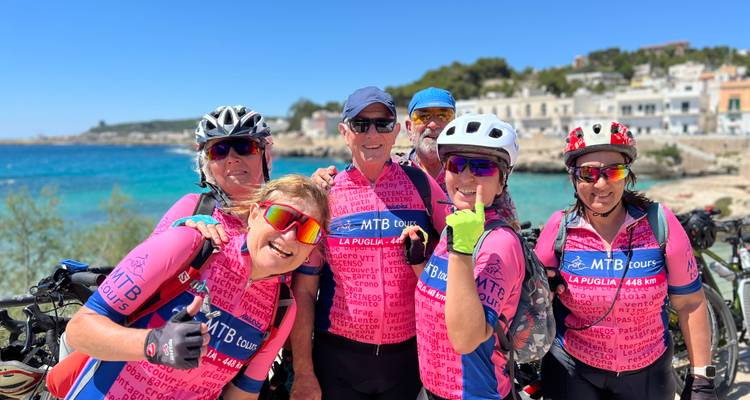 Des cyclistes souriants posent ensemble au bord d'une mer turquoise et d'un charmant port italien.