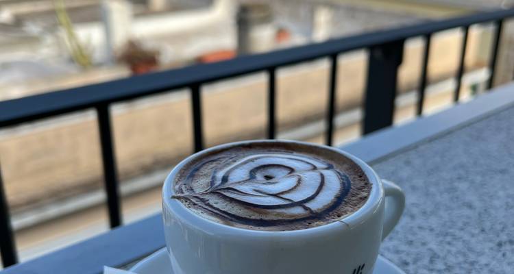 Gros plan d'un cappuccino avec tourbillon de chocolat décoratif sur une table de café en plein air.