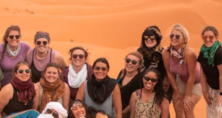 Un grupo turístico alegre de mujeres con gafas de sol posa entre las ondulantes dunas del Sahara.