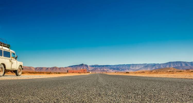 Una larga carretera desierta del desierto se extiende hacia cordilleras montañosas distantes bajo un cielo azul sin nubes.