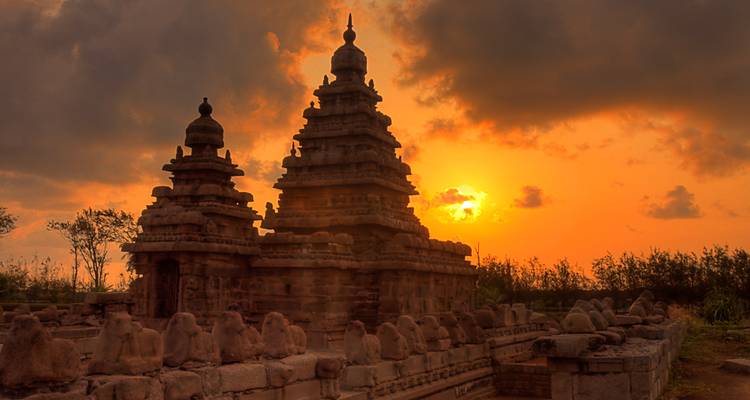Les sanctuaires jumeaux du Temple du Rivage se découpant en silhouette contre un ciel de coucher de soleil orange lumineux.