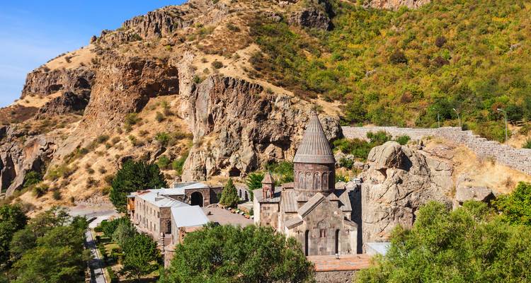 Monastère de pierre médiéval niché contre des falaises rocheuses spectaculaires et des collines boisées parsemées de clairières.