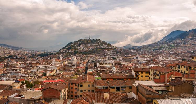 Vue panoramique du centre historique de Quito s'étendant sous la colline El Panecillo sous un ciel dramatique.
