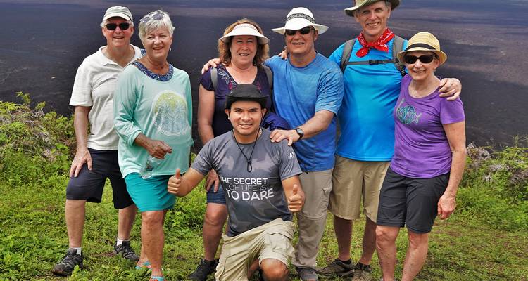 Wandelaars glimlachen voor een groepsfoto op weelderige vulkanische hellingen met donkere krater op de achtergrond.