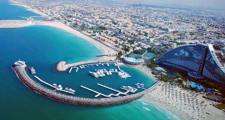 Luchtfoto van de kustlijn van Dubai met turkooizen zee, marinadokken en het golffvormige Jumeirah Beach Hotel.