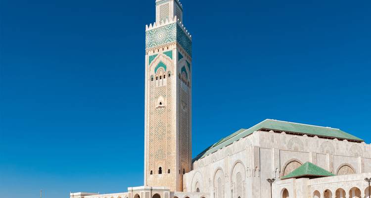 Alto minarete y fachada de la Mezquita Hassan II erguidos bajo un cielo azul impecable.