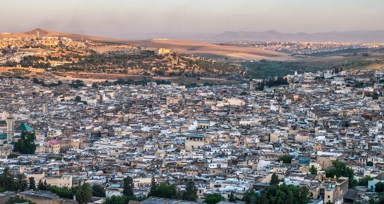 Vista aérea expansiva de la medina densamente poblada de Fez extendiéndose por un valle al atardecer.