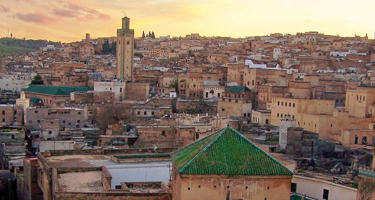 Altstadt von Fes in warmen Sonnenuntergangstönen getaucht mit einem hohen Minarett mit grünem Dach, das über die Dächer emporragt.