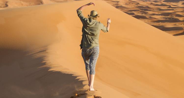 Un viajero solitario equilibrándose descalzo a lo largo de la cresta de una duna de arena dorada en el desierto.