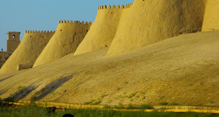Section de murs défensifs en adobe éclairés par le soleil avec des créneaux arrondis dans le désert