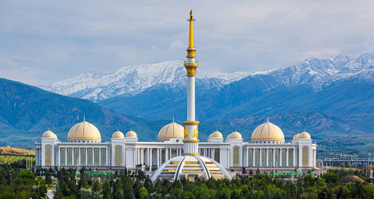 Grand white marble palace with a tall golden spire framed by snow-capped mountains