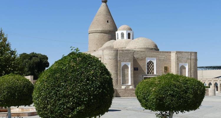 Historic mausoleum complex with rounded tower and manicured topiary trees in foreground