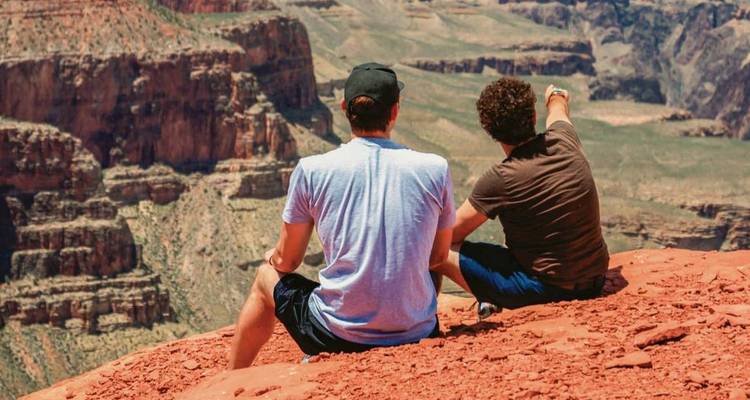 Twee reizigers zittend op een rood zandstenen richel met uitzicht op de uitgestrekte Grand Canyon.
