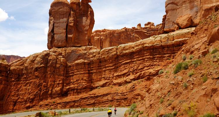 Les cyclistes roulent le long d'une route bordée de formations rocheuses rouges stratifiées spectaculaires