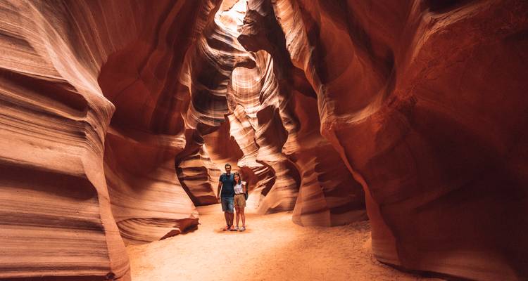 Un couple se tient dans les murs de grès tourbillonnants d'Antelope Canyon éclairés par de doux rayons