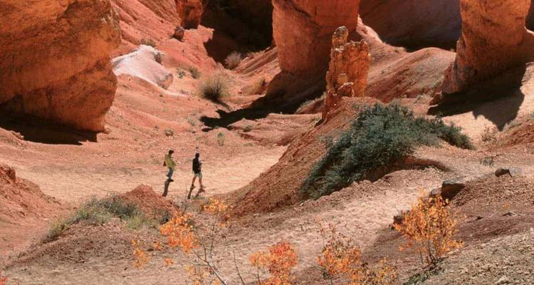 Deux randonneurs marchant à travers des formations de hoodoos en grès rouge dans un canyon désertique ensoleillé.
