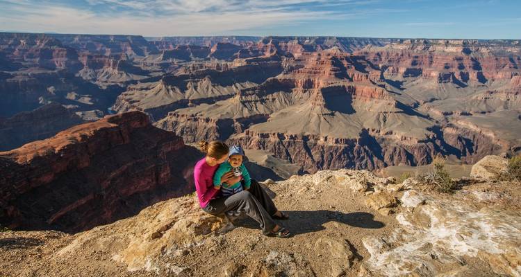 Moeder en jong kind zitten op een rotsrichel en bewonderen de uitgestrekte lagen van de Grand Canyon.