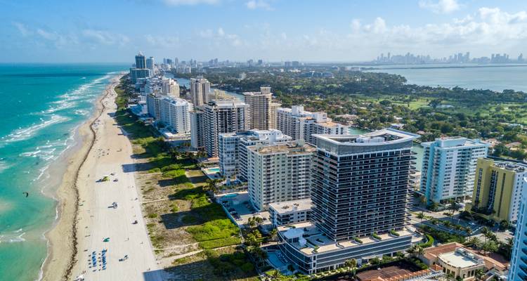 Vue aérienne le long de Miami Beach avec des hôtels de grande hauteur bordant le rivage de sable blanc et les eaux turquoise de l'Atlantique s'étendant jusqu'à l'horizon.