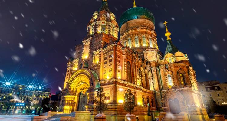 Illuminated Saint Sophia Cathedral in Harbin at night with falling snow creating a magical scene.