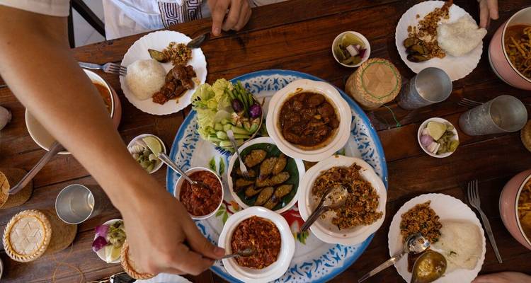 Overhead view of a shared table filled with traditional dishes, dips, and vegetables as hands reach in.
