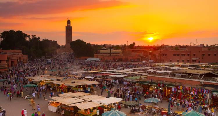 Bustling Jemaa el-Fnaa square at sunset with the Koutoubia Mosque silhouetted against an orange sky.