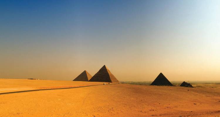 Eine weite Sandebene erstreckt sich in Richtung der fernen Pyramiden unter dem sanften Glanz des späten Tageslichts.