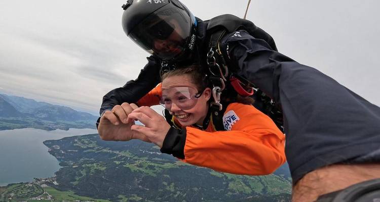 Des parachutistes en tandem chutent librement au-dessus d'un lac suisse et de champs en damier, sourires éclatants d'adrénaline.