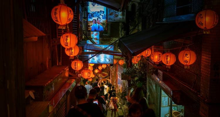 Ruelle étroite éclairée par des lanternes grouillante de visiteurs dans un vieux marché à flanc de colline après la tombée de la nuit