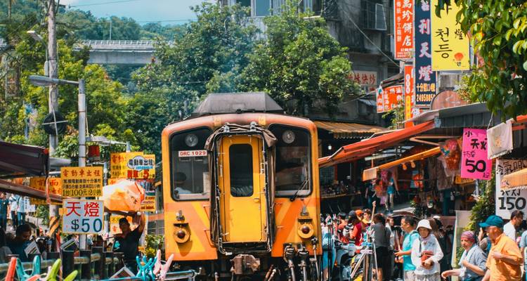 Train local jaune vif traversant une rue de marché animée bordée d'enseignes colorées