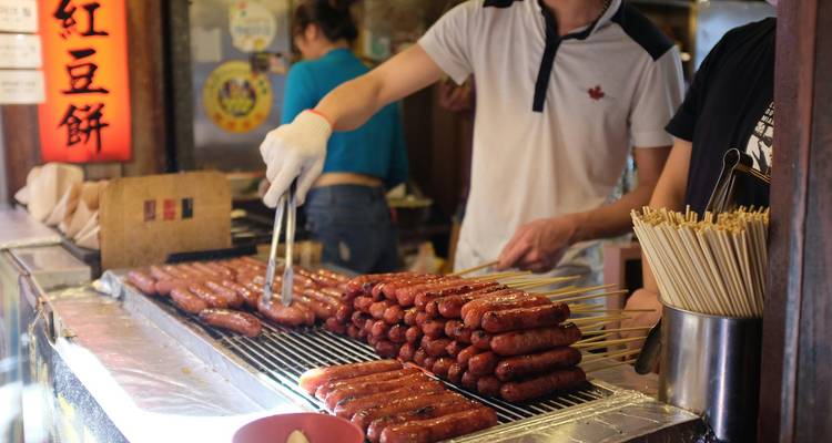 Vendeurs de street-food grillant des saucisses en brochettes à un stand de marché