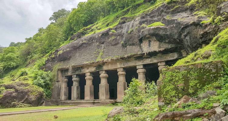 Entrée de temple rupestre avec rangée de piliers de pierre massifs intégrés dans une falaise verdoyante