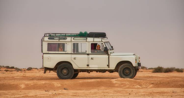 Vehículo todoterreno blanco estacionado en terreno desértico plano con un conductor visible a través de la ventana.