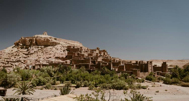 El histórico ksar de tierra de Ait Benhaddou se alza sobre un exuberante oasis verde bajo un cielo azul despejado.