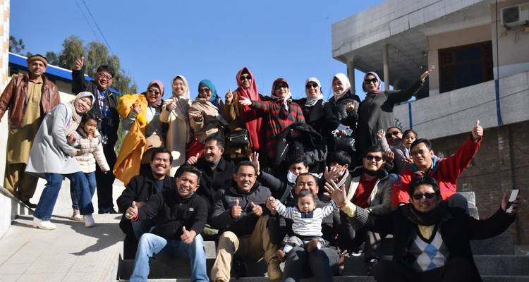 Grand groupe de touristes joyeux posant sur des marches extérieures en faisant des gestes de pouces levés.