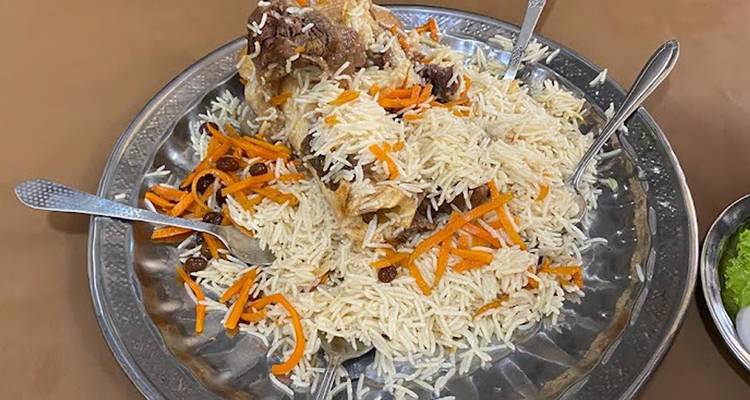 Grand plat en métal de riz pilaf avec des morceaux de viande, des carottes et des raisins secs.