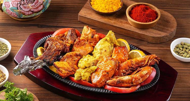 Plato mixto colorido de mariscos con langostinos y pescado tandoor en plancha de hierro caliente rodeado de especias.