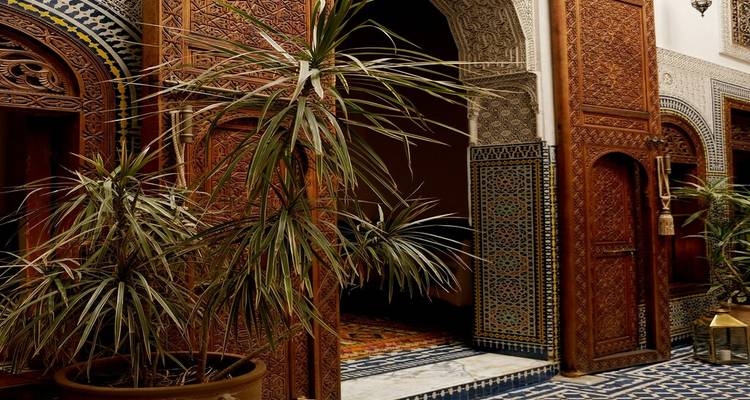 Intérieur de riad marocain orné avec portes en bois sculpté, carreaux de mosaïque et plante en pot.