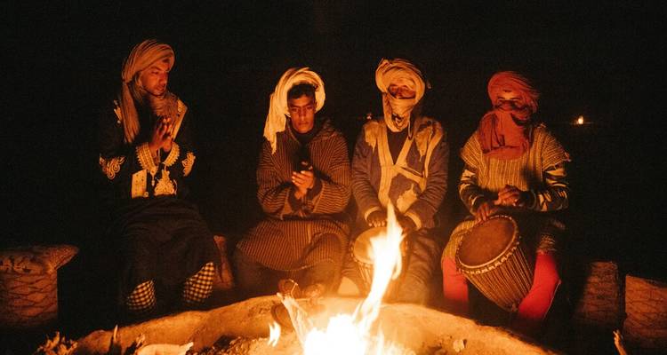 Musiciens berbères en tenue traditionnelle jouant du tambour et priant autour d'un feu de camp la nuit.