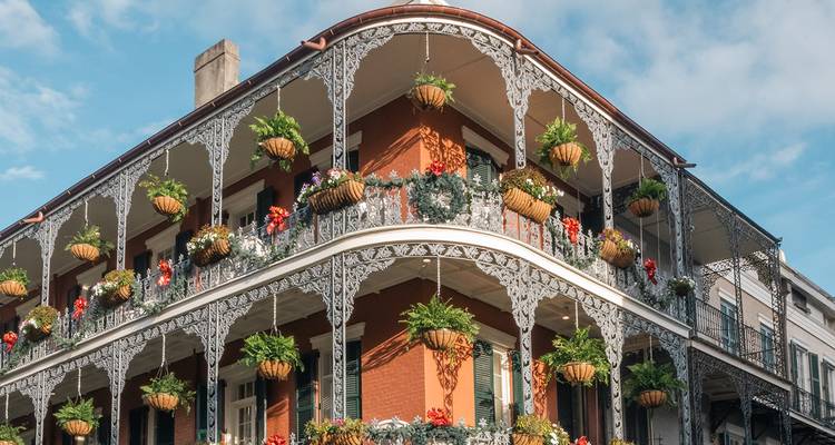 Balcones de hierro forjado ornamentados rebosantes de plantas colgantes en un edificio clásico del Barrio Francés