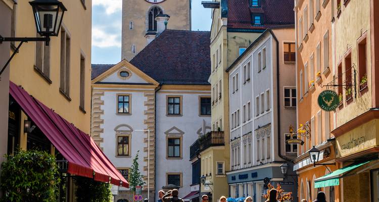 Rue colorée de la vieille ville de Ratisbonne avec tour de l'horloge et cafés en plein air animés de visiteurs.