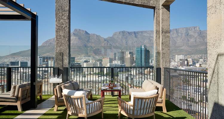 Terrasse de toit élégante avec canapés donnant sur un horizon urbain et la montagne de la Table en arrière-plan.