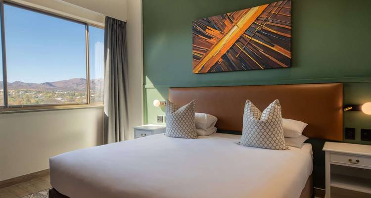 Chambre d'hôtel moderne avec mur d'accent vert, grande fenêtre et vue sur la montagne.