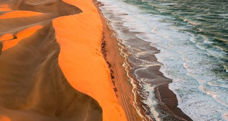 Spectaculaire vue aérienne où d'imposantes dunes de sable orange plongent directement dans les vagues de l'Atlantique.