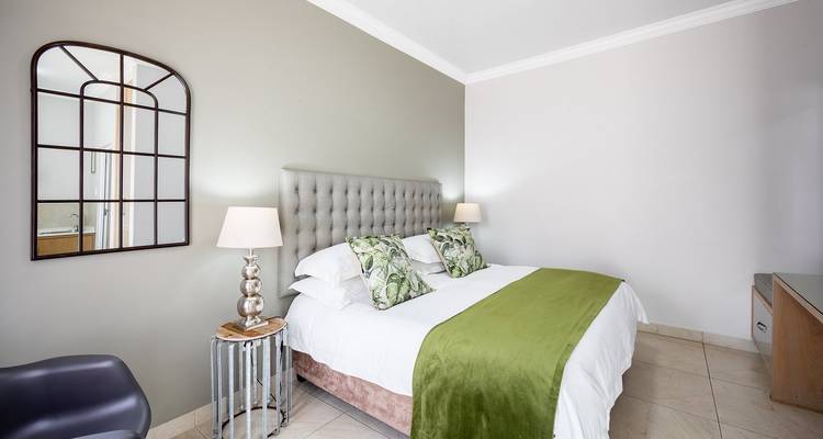 Chambre à coucher minimaliste avec tête de lit capitonnée, plaid vert et éclairage doux.