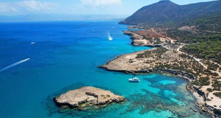 Aerial panorama of a rugged Mediterranean coastline with crystal-clear blue water and small islet