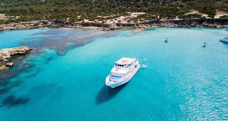 White excursion boat cruising on bright blue lagoon waters near a forested shore