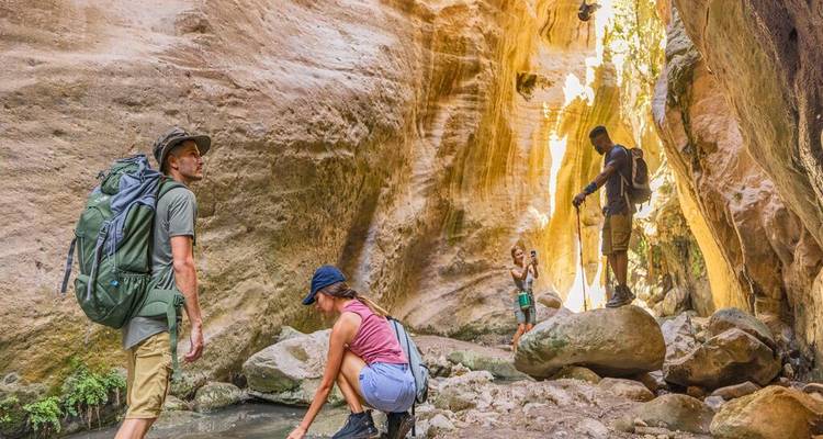 Hikers exploring a narrow sandstone canyon with sunlight streaming onto the rocky floor