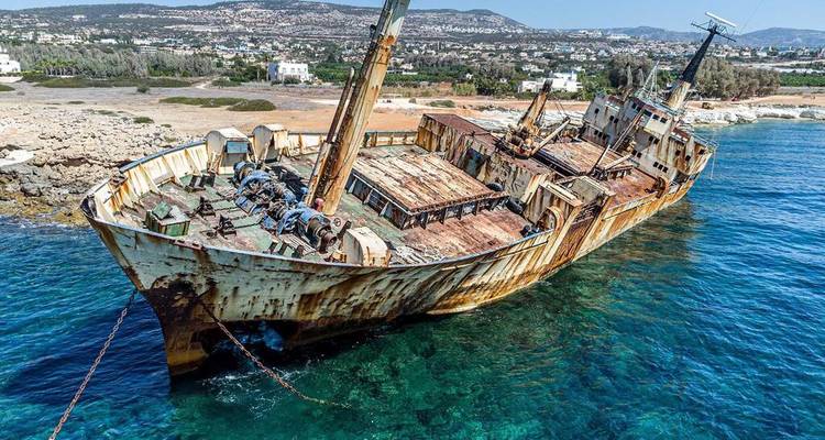 Rusting cargo shipwreck grounded on shallow turquoise waters near rocky shore